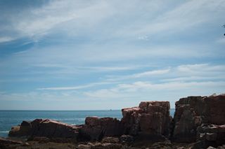 Photography by Keagen Thomson at Acadia's Thunder hole, a view of a rocky shore against the sea and blue sky horizon