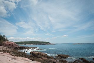 Photography by Keagen Thomson at Acadia's Thunder hole, a view of the ocean horizon and a forested island from a rocky coast